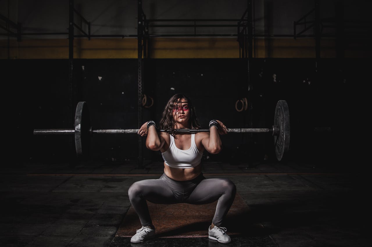 A strong female weightlifter squats with a barbell in a dimly lit gym, showcasing power and fitness.